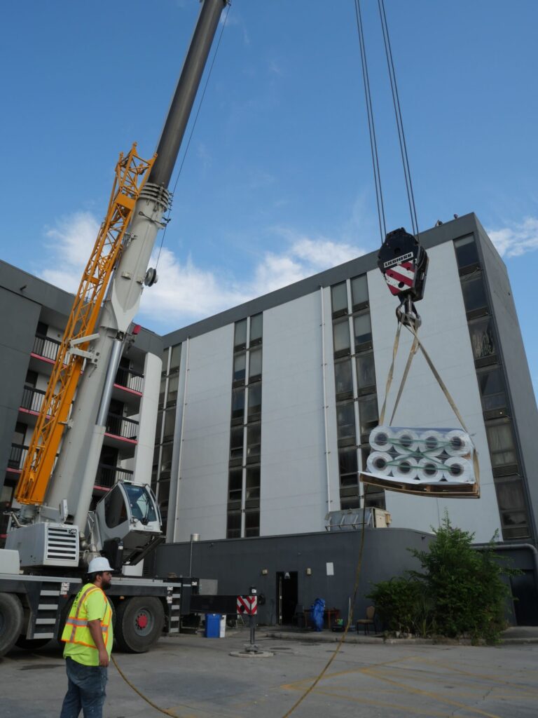 A crane lifting rolls of roofing membrane up to a multi-storey building during a re-roof