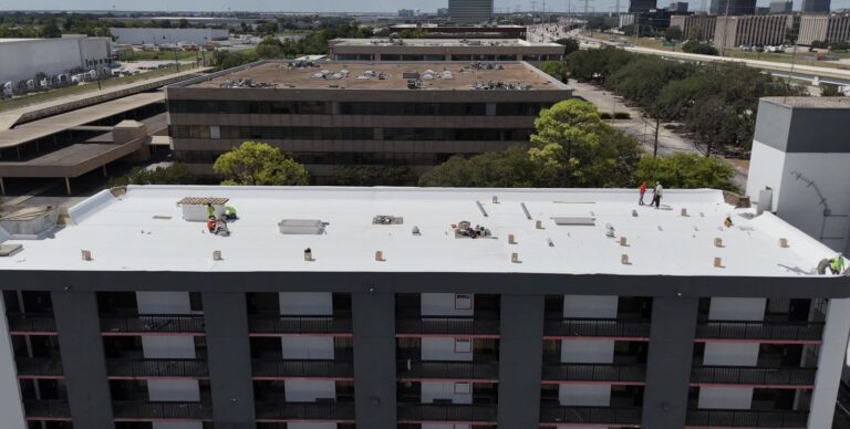 Aerial view of crew members working across a finished white flat roof on a multi-storey building