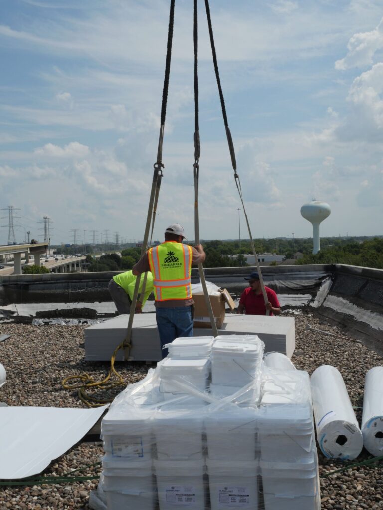 A Pineapple crew member guiding a crane load of roofing materials onto a commercial roof deck