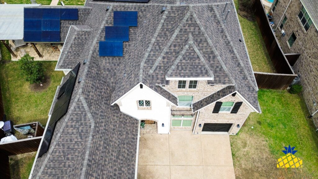 Aerial view of a two-storey brick home with an asphalt shingle roof and rooftop solar panels in North Texas